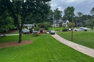 In Midtown Atlanta, workers and vehicles bustle on a residential street with landscaping equipment. They're engaged in trenchless sewer line repair near two modern houses, all framed by lush trees.