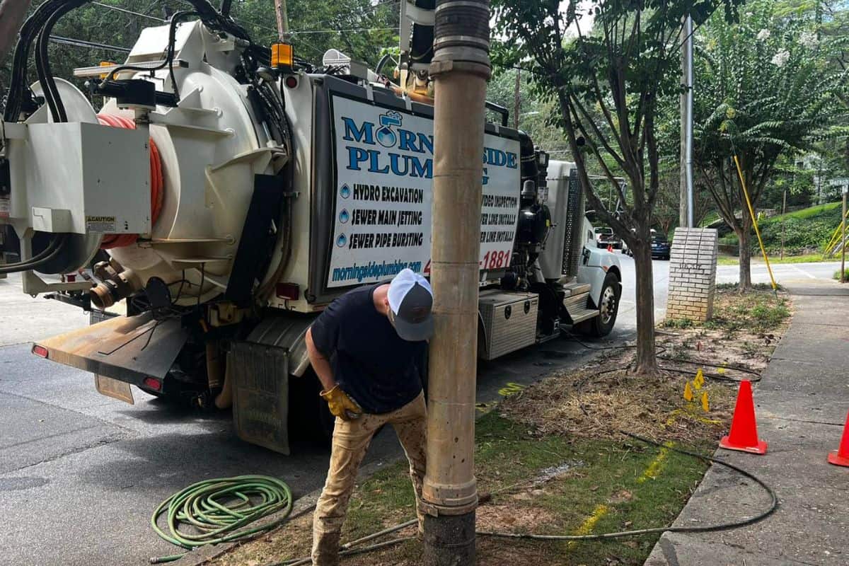 Worker operating a vacuum truck on a sidewalk, with orange cones marking the area.