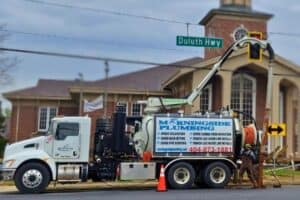 A Morningside Plumbing truck is parked on Duluth Hwy with two workers handling equipment. A church is visible in the background.