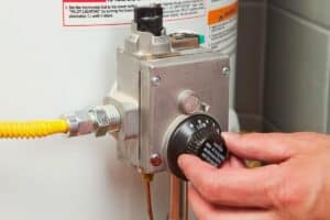 Adjusting the thermostat on a water heater with a control knob labeled "Low" to "High." For those in need of water heater repair near me Atlanta, ensure your device operates efficiently by handling settings carefully.