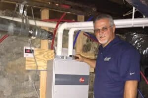 In a basement in Brookhaven, a man in a blue shirt operates a boiler, surrounded by pipes and ducts. Nearby, a display screen shows the number 118, highlighting the efficiency often seen with tankless water heater benefits in such setups.