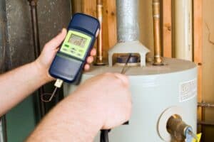 A technician in Buckhead checks a water heater's emissions with a handheld gas analyzer. The display shows readings as the probe slides into the exhaust, while surrounding pipes and walls are clearly visible in the background, ensuring efficient water heater repair.