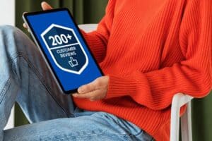 Person holding a tablet displaying a blue screen with a shield icon, "200+ Customer Reviews," and a thumbs-up—showcasing why they're recognized as the best Midtown Atlanta plumber.